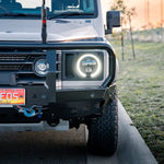 Front view of a white off-road vehicle with glowing headlights on a grassy area.