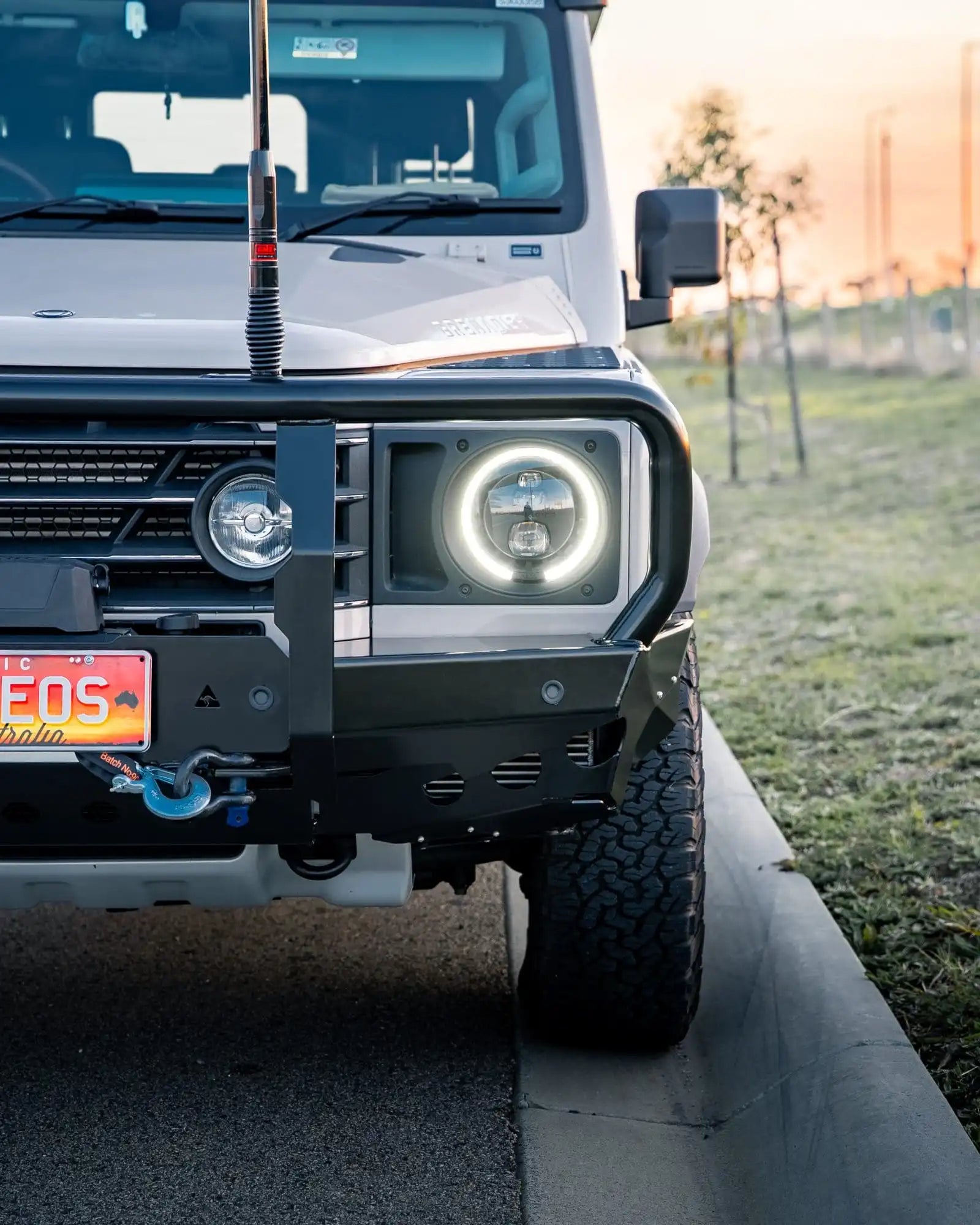 Front view of a white off-road vehicle with glowing headlights on a grassy area.