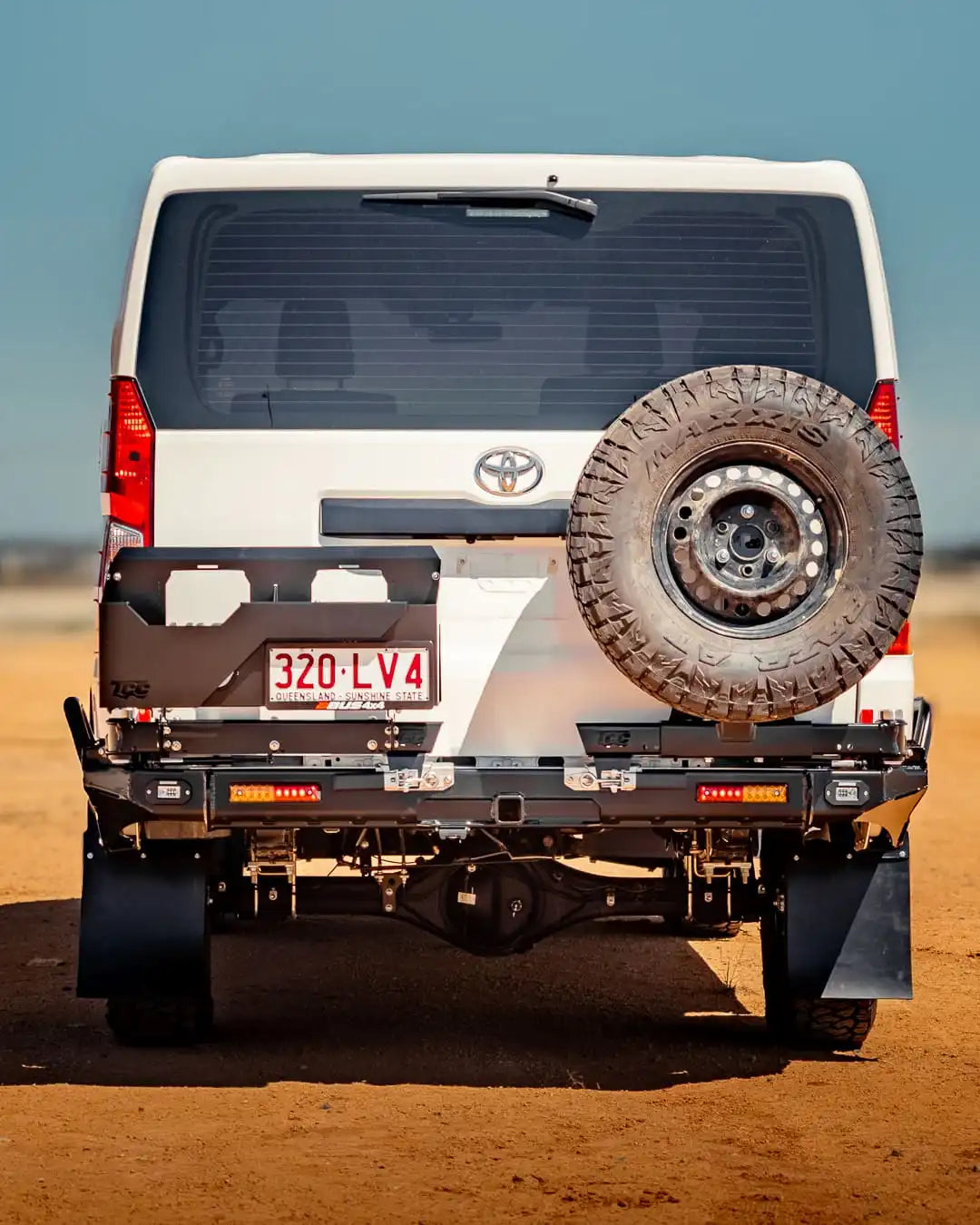 Back view of a white Toyota vehicle with a spare tire on a desert landscape
