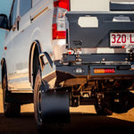 Close-up of a white van's rear with a black bumper on a dirt road.