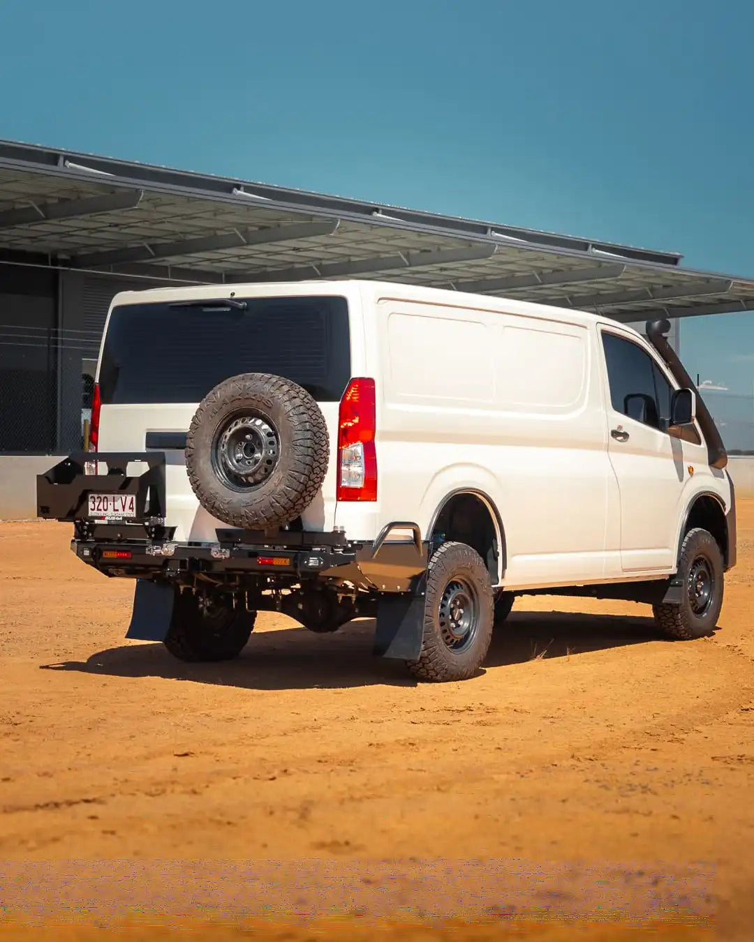 White van with off-road modifications on a dirt road under a clear blue sky.