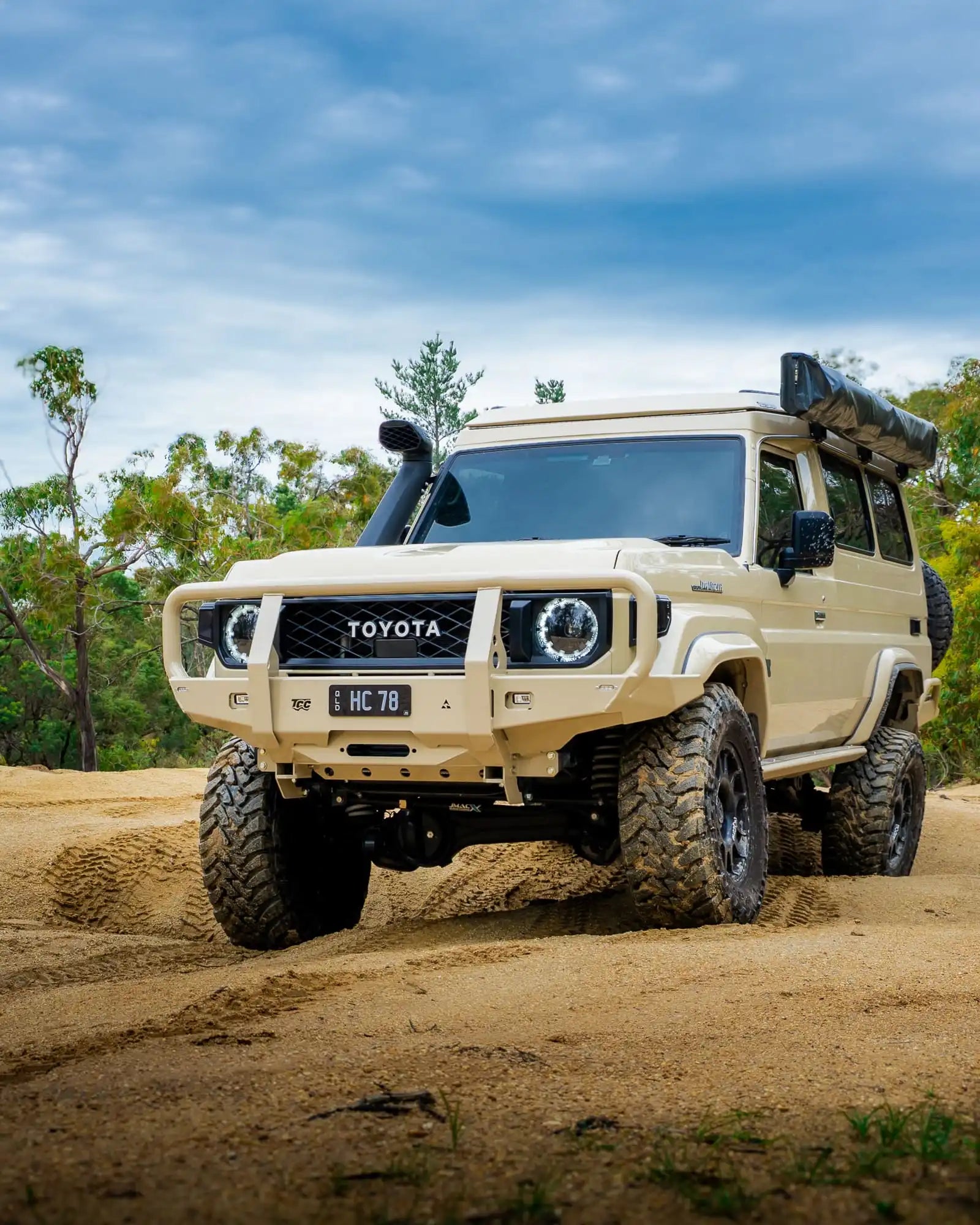 sandy Toyota off-road vehicle on a dirt road with trees in the background