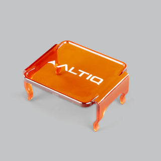 Amber ALTIQ DX4 lens cover seen from above at an angle, the translucent orange panel with the ALTIQ name across it and four moulded clips reaching down from the corners