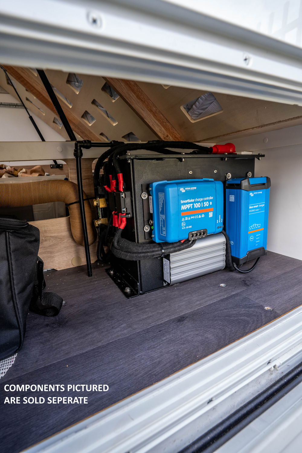 The compartment mounted on its side under a bed platform in a van, with a Victron SmartSolar MPPT 100/50 charge controller and a Victron Blue Smart charger fixed to its outer face