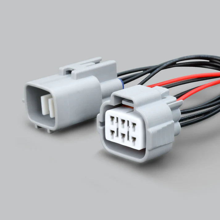 The two grey headlight connectors side by side, one showing its blade pins and the other its six-cavity socket face, with red and black leads running away behind