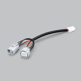 The Isuzu piggy-back adaptor laid out complete, two grey vehicle connectors at one end joined by a corrugated sleeve to a small white plug at the other