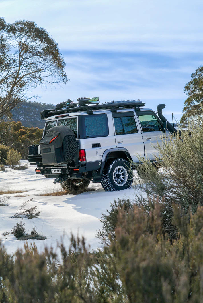 4x4 vehicle on a snowy road with trees and mountains in the background