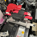 Close-up of a car battery with cables attached, showing labels and warning stickers.