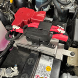 Close-up of a car battery with cables attached, showing labels and warning stickers.