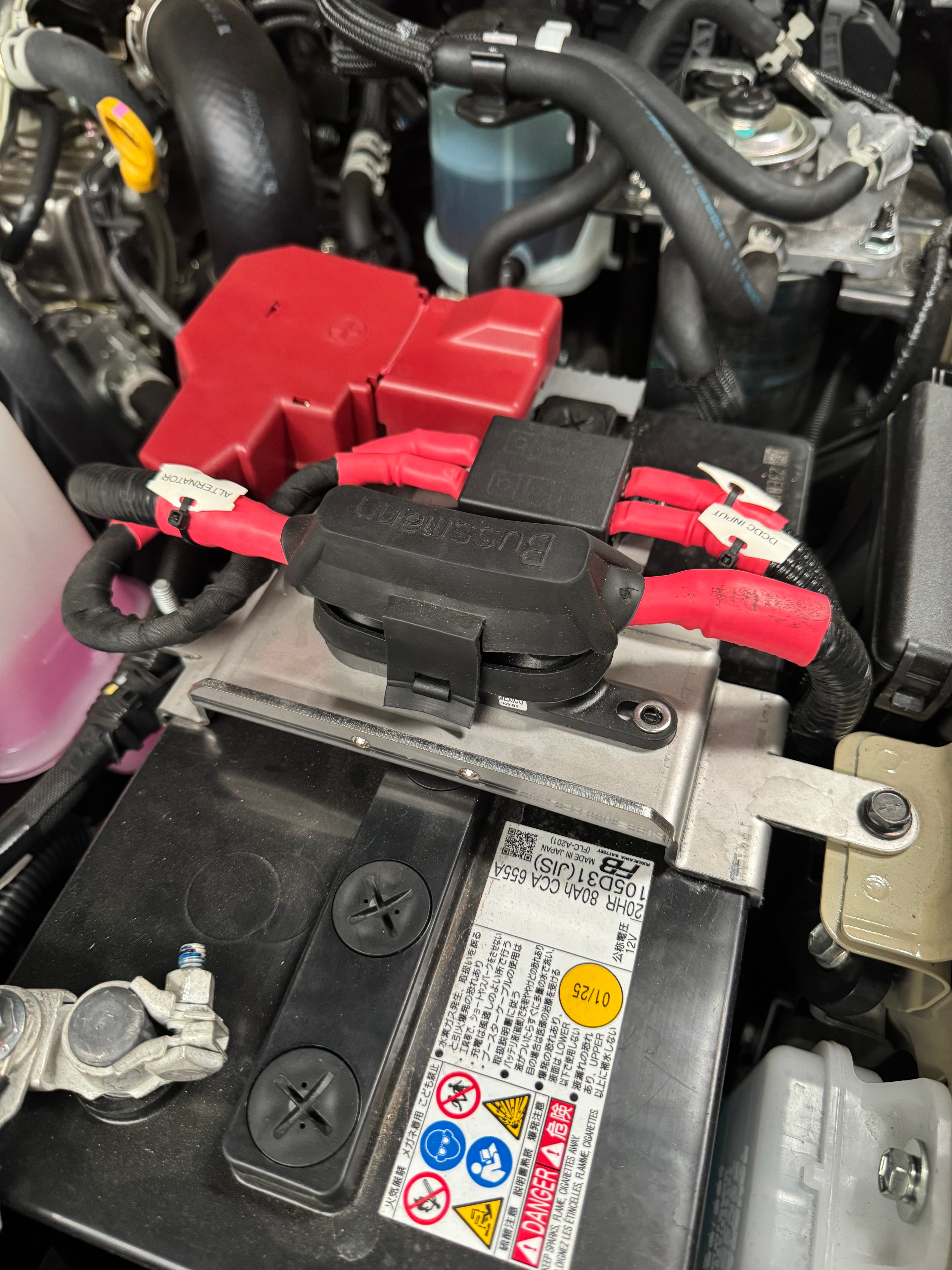 Close-up of a car battery with cables attached, showing labels and warning stickers.