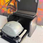 Black barbecue grill with a lid open, showing a portable barbecue inside, against a colorful abstract background.