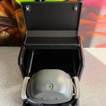 Portable grill with lid open on a concrete floor, with a colorful background.