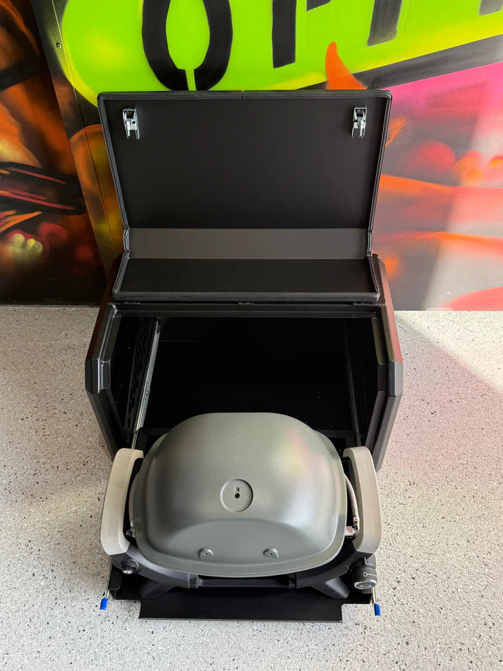 Portable grill with lid open on a concrete floor, with a colorful background.