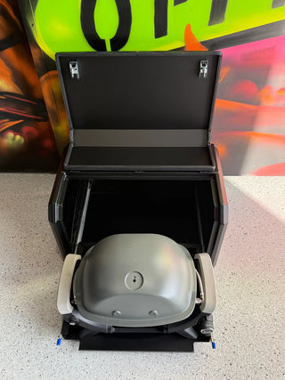 Portable grill with lid open on a concrete floor, with a colorful background.