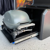 Portable grill with a hose attached inside an open toolbox on a concrete surface.