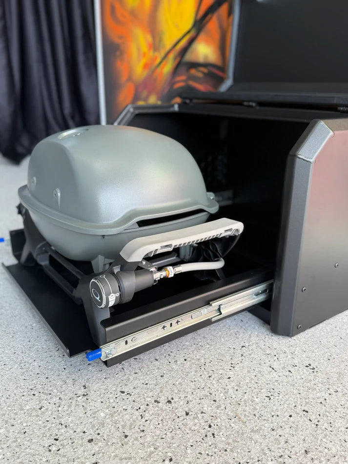 Portable grill with a hose attached inside an open toolbox on a concrete surface.
