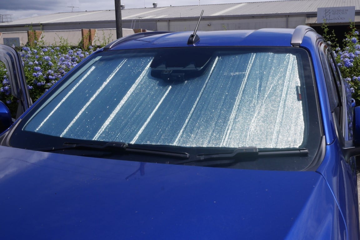 Blue car with a sunshade covering the windshield, parked outdoors.