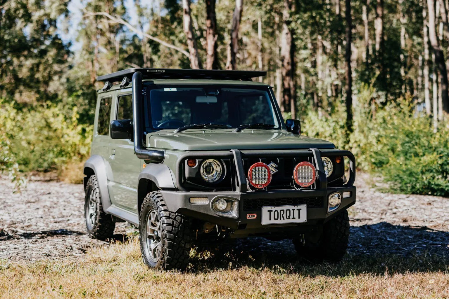 Green off-road vehicle with 'TORQIT' license plate in a forest setting