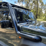 Close-up of a vehicle's windshield and side mirror with trees in the background