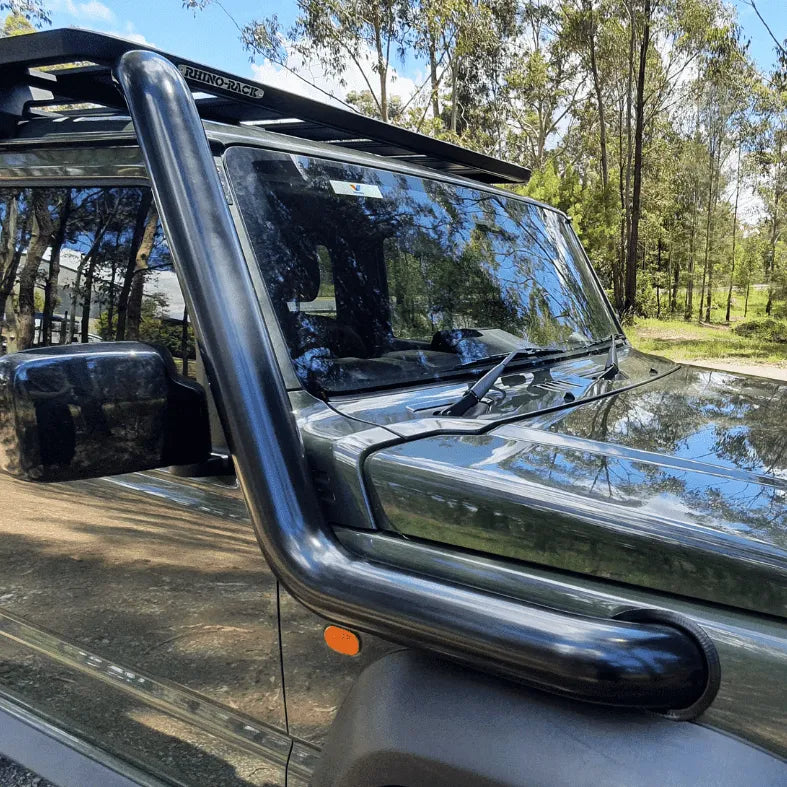 Close-up of a vehicle's windshield and side mirror with trees in the background
