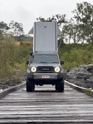 Toyota truck with a camper shell on a wooden bridge in a natural setting