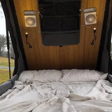Bed inside a camper van with wooden paneling and curtains, outdoors.