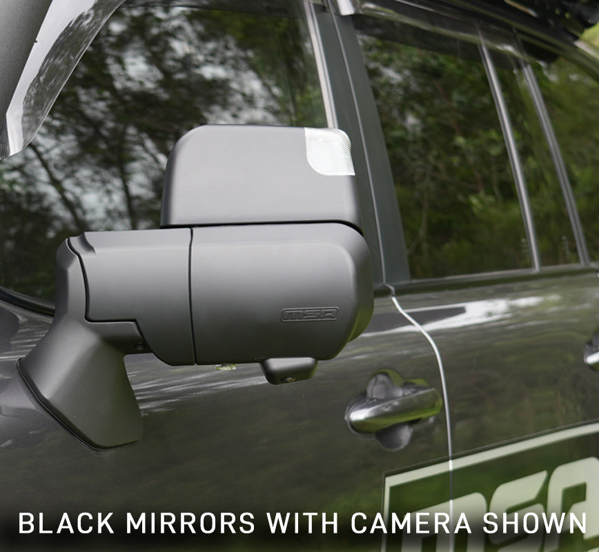 Car side mirror with built-in camera on a vehicle, surrounded by greenery.