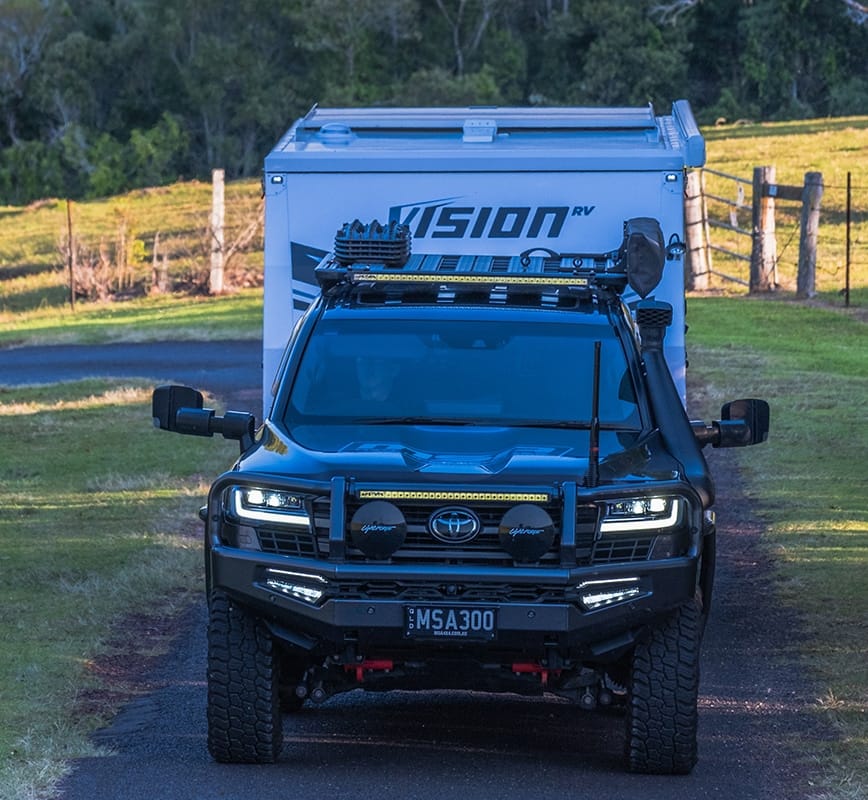 Black Toyota SUV with a Vision camper shell parked on a dirt road.