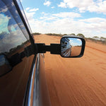 Side view mirror of a vehicle on a desert road with blue sky and clouds.