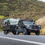 Black SUV towing a green camper trailer on a road with a mountainous background