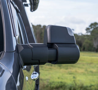 MSA Power Fold towing mirror fitted to a dark 4WD, seen from behind and to the side, the arm extended out past the body with the indicator lens in the mirror head and open paddock behind