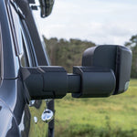 Side view of a vehicle with extended towing mirrors in an outdoor setting.