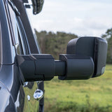 Side view of a vehicle with extended towing mirrors in an outdoor setting.