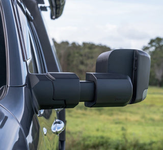 Side view of a vehicle with extended towing mirrors in an outdoor setting.