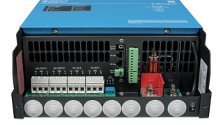 Underside connection bay of a Victron Quattro-II with the cover removed, showing the AC-IN-1, AC-IN-2, AC-OUT-1 and AC-OUT-2 terminal blocks, the VE.Bus sockets and the red and black battery studs