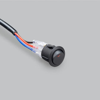 Round black rocker switch with a red illuminated dot, wired with red, blue and black leads through clear insulated crimp connectors into a black sheathed lead