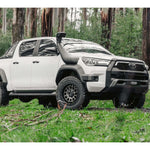 White Toyota truck with black off-road tires in a forest setting with Safari FLARE KIT