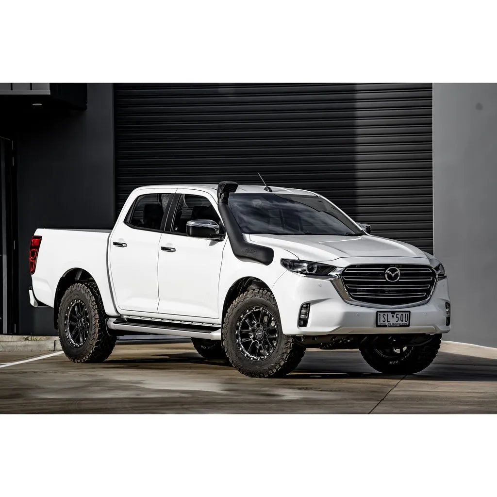 White Mazda pickup truck with black wheels parked in front of a gray garage door.