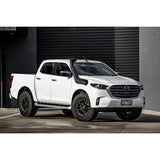 White Mazda pickup truck with black wheels parked in front of a gray garage door.