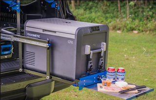 A Dometic CFX fridge strapped to an MSA drop slide, pulled out of a ute canopy and dropped down, with the fold-out table beside it holding drinks, dip and a cheese board