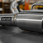 Stainless steel exhaust pipe with 'torqit' branding on a blurred background