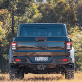 Back view of a black Jeep truck in a natural setting with trees and grass.
