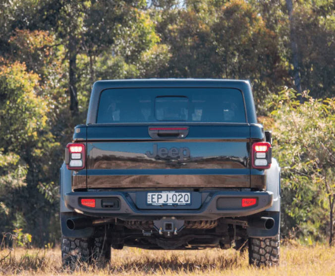 Back view of a black Jeep truck in a natural setting with trees and grass.