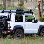 White SUV with roof rack and spare tire in a natural setting