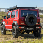 Red Suzuki truck with off-road tires and roof rack in a natural setting