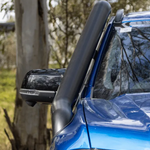 Close-up of a blue vehicle's side mirror and snorkel with trees in the background