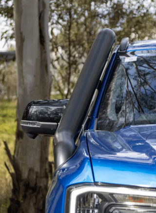 Close-up of a blue vehicle's side mirror and snorkel with trees in the background