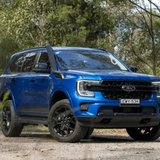 Blue Ford SUV parked on a dirt road with trees in the background