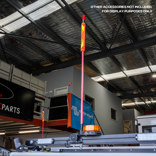 The 1.2m whip fitted to a vehicle roof rack in a workshop, the red fibreglass shaft rising to an illuminated amber LED top, with an amber rotating beacon mounted alongside. Caption on the image reads other accessories not included, for display purposes only