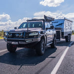 SUV towing a camper trailer on a road with a clear sky.